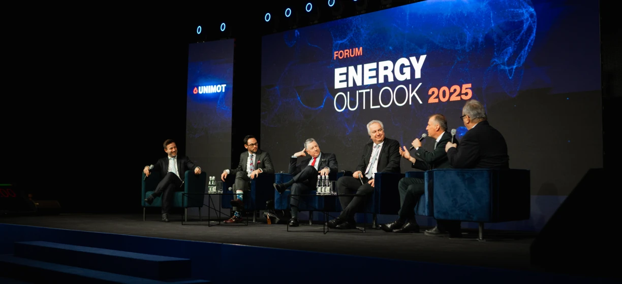 Pracownik biurowy w garniturze stoi na scenie pronuncjując przemowę podczas wydarzenia publicznego forum UNIMOT Energy Outlook 2025.
