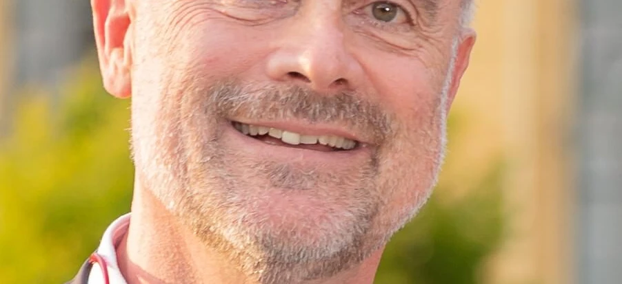 A close-up of a person's face with a big smile, chin resting on their hand, showing happiness and wrinkles on their forehead.