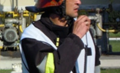 A blue-collar worker wearing personal protective equipment including a helmet and high-visibility clothing. The image shows an emergency service worker, possibly a firefighter, in their work uniform.