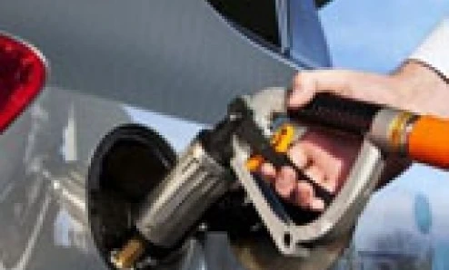 A fuel dispenser at a filling station next to a car with its door open and a windshield being cleaned. Automotive care with electric vehicle and hood in background.