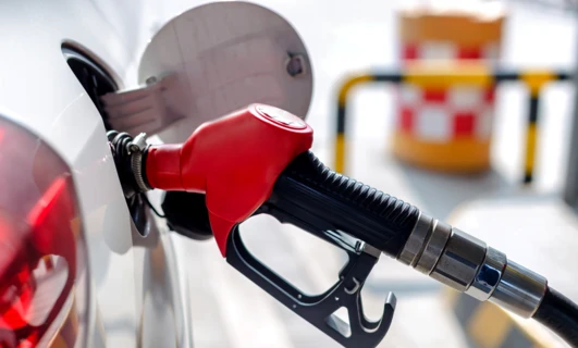 Dystrybutor paliwa na stacji benzynowej z dyszą i wężem, gotowy do tankowania benzyny lub oleju napędowego. Pokazana jest również stacja ładowania pojazdów elektrycznych.