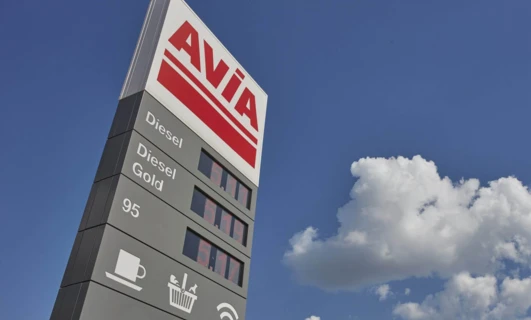 A close-up of a gold AVIA fuel pump with diesel options and automotive side-view mirrors in the background.