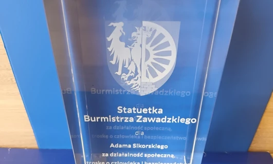 Award for Adam Sikorski for his social activity, care for people, and safety. Gmina Zawadzkie banner with VIT graphics.