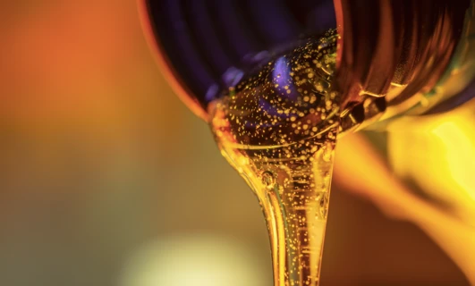 Close-up macro photography of flowing yellow and orange liquid resembling motor oil or cooking oil, with a focus on the texture and movement of the fluid.