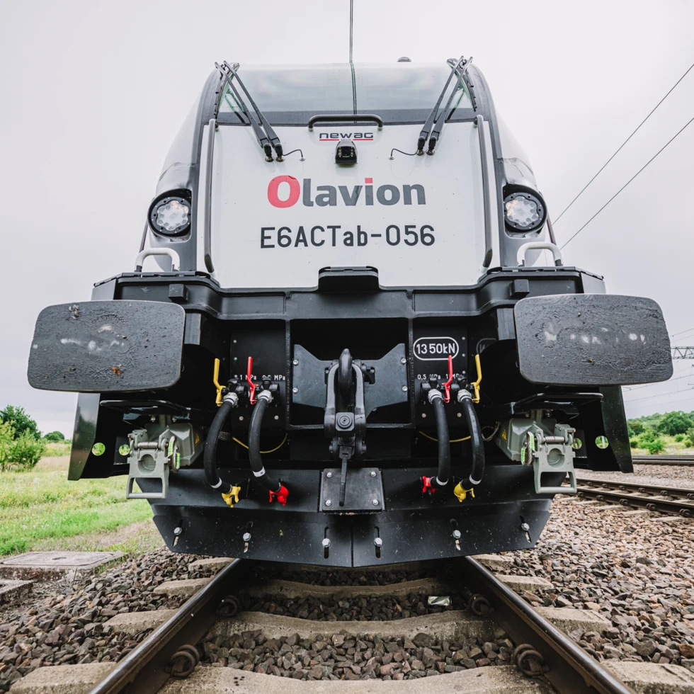 Elektryczna lokomotywa E6ACTab-056 firmy Newag porusza się po torach z pracującymi wycieraczkami przedniej szyby, będąc symbolem efektywności nowoczesnego transportu kolejowego. Transport publiczny w ruchu, prezentujący moc i nowoczesny design nowego taboru kolejowego.