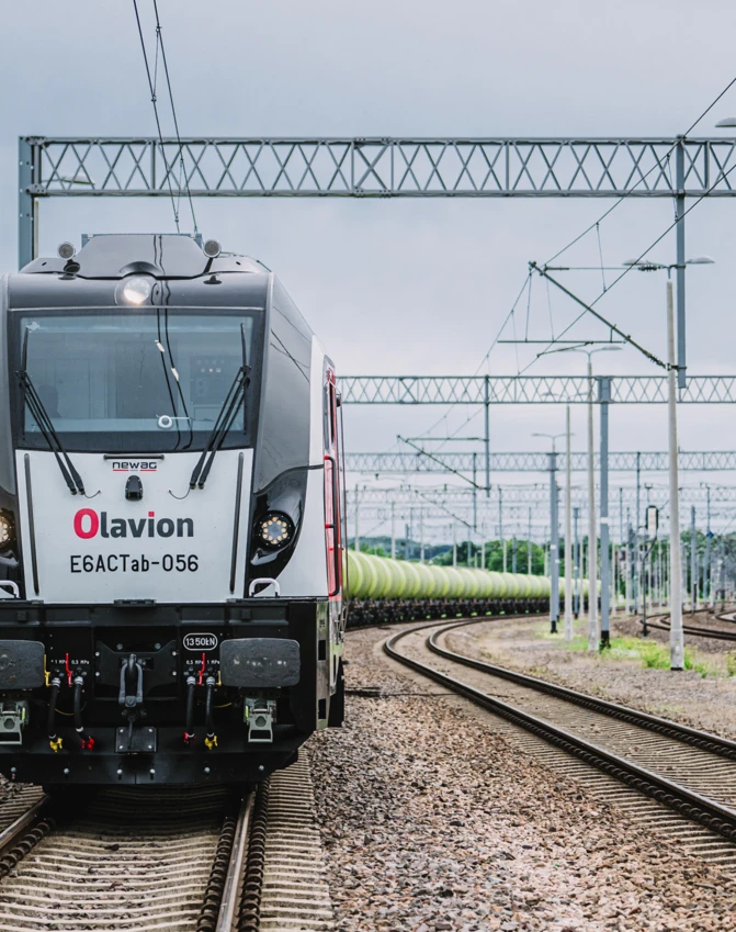 Obraz nowej lokomotywy Olavion E6ACTab-056 na torach kolejowych, środek transportu wykorzystujący tabor. Ten żelazny potwór o mocy 1350 kN jest gotowy do efektywnego świadczenia usług transportu publicznego.